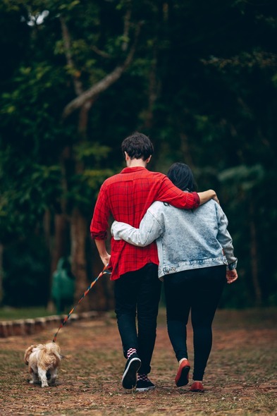 Couple with arms around each other walking a dog on a lead