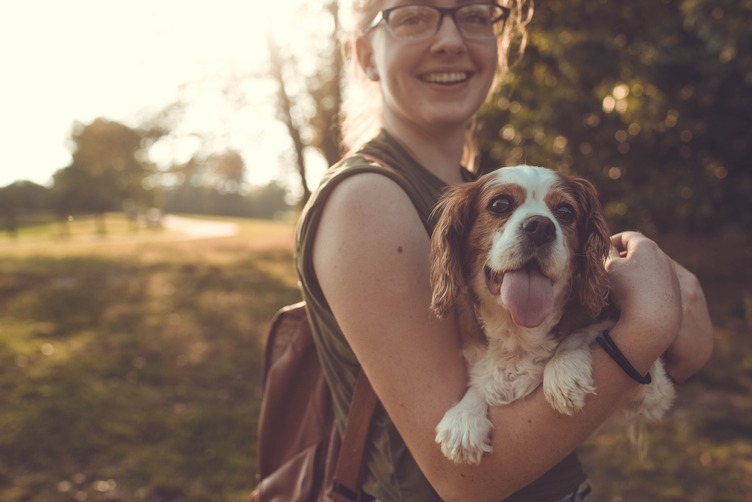 Young woman holding her dog with a great afternoon sunlit background